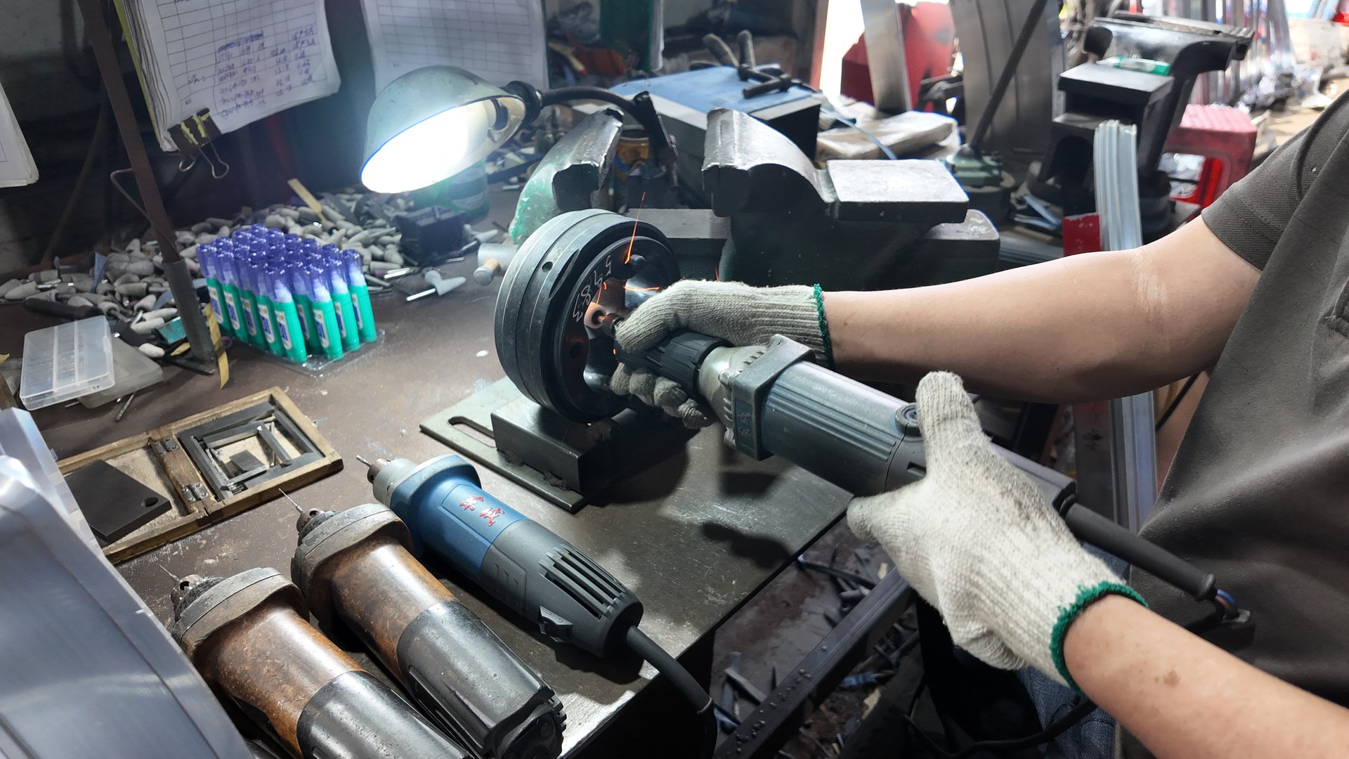 A worker using a hand tool on a die at the tooling workbench
